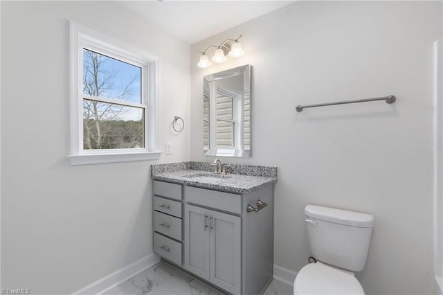 half bath with marble finish floor, toilet, vanity, and baseboards