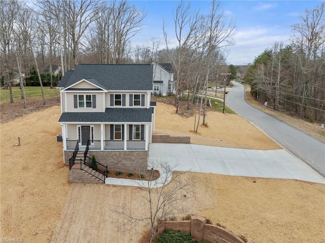 traditional-style house featuring aphalt driveway, covered porch, and a shingled roof