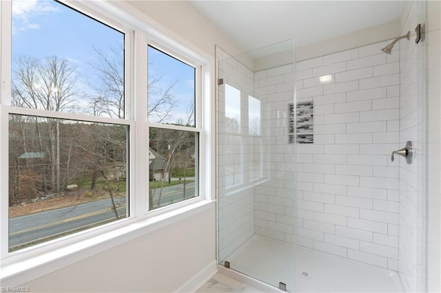 bathroom featuring a wealth of natural light, baseboards, tiled shower, and marble finish floor