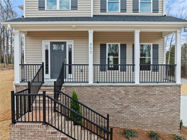 view of exterior entry with covered porch and a shingled roof