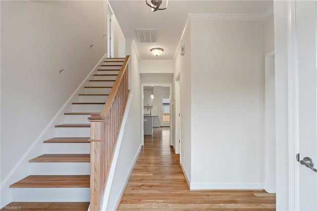 stairs with baseboards, wood finished floors, visible vents, and ornamental molding