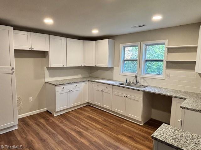 kitchen with light stone countertops, sink, dark wood-type flooring, and white cabinets