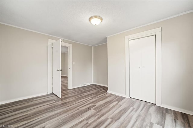 unfurnished bedroom with light hardwood / wood-style floors, a textured ceiling, a closet, and ornamental molding