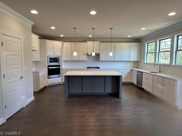 kitchen with white cabinets, hanging light fixtures, sink, crown molding, and a kitchen island