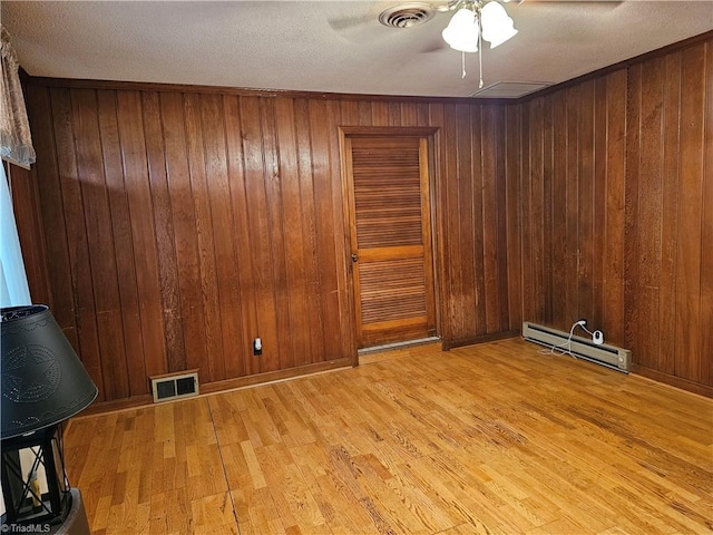4875 Follansbee Rd, Winston-Salem, NC 27127 - empty room with a baseboard heating unit, ceiling fan, light wood finished floors, wood walls, and a textured ceiling