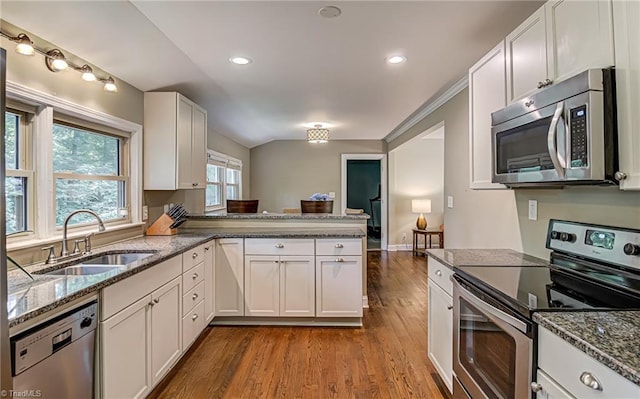 kitchen featuring appliances with stainless steel finishes, a peninsula, light wood-type flooring, white cabinetry, and a sink