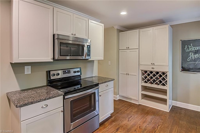 kitchen featuring stainless steel appliances, dark stone countertops, wood finished floors, and white cabinetry