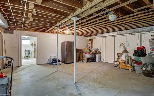 unfinished below grade area featuring concrete block wall and freestanding refrigerator