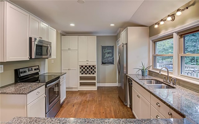 kitchen featuring light wood-style flooring, appliances with stainless steel finishes, stone countertops, white cabinets, and a sink