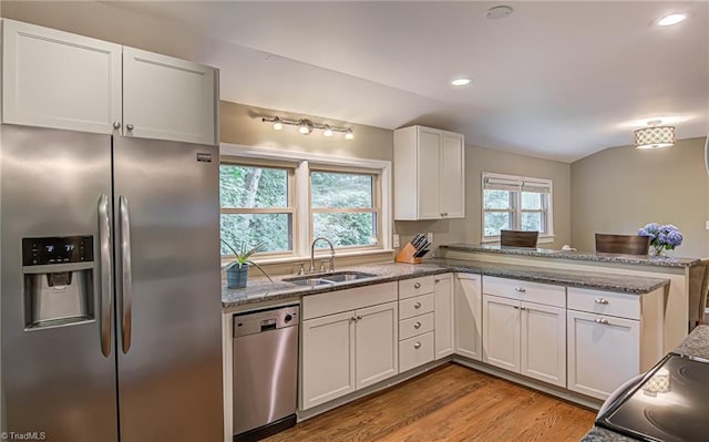 kitchen with stainless steel appliances, white cabinetry, a sink, light stone countertops, and a peninsula