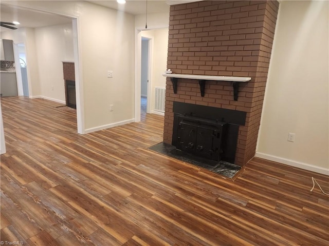 unfurnished living room featuring a brick fireplace, visible vents, dark wood finished floors, and baseboards