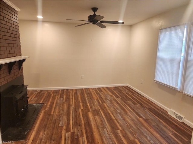 unfurnished living room with dark wood finished floors, visible vents, a wood stove, ceiling fan, and baseboards