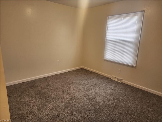 unfurnished room featuring dark colored carpet, visible vents, and baseboards