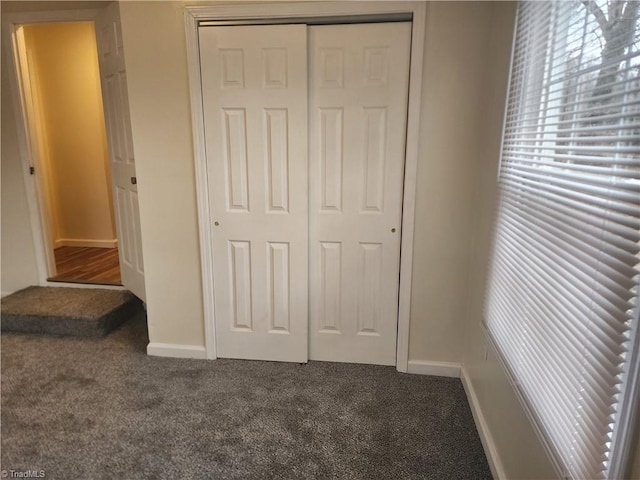 unfurnished bedroom with dark colored carpet, a closet, and baseboards