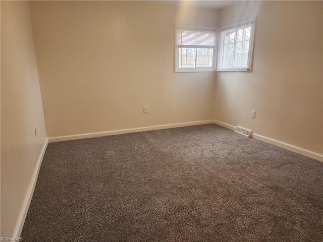 unfurnished room featuring visible vents, dark carpet, and baseboards