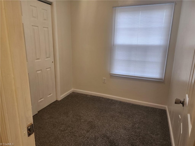 unfurnished room featuring baseboards and dark carpet