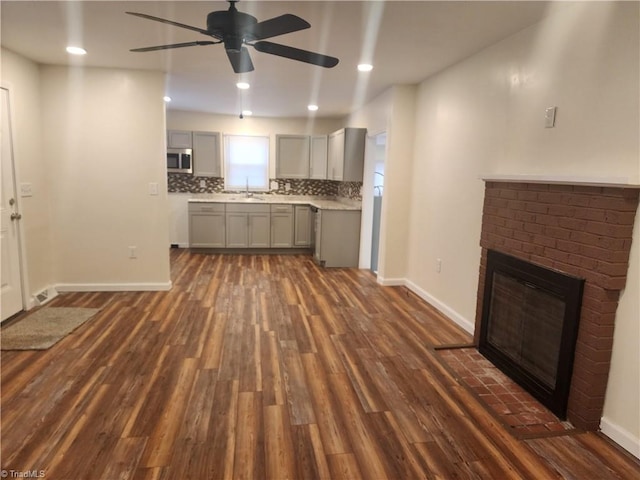 kitchen with dark wood-style floors, light countertops, stainless steel microwave, gray cabinetry, and a brick fireplace