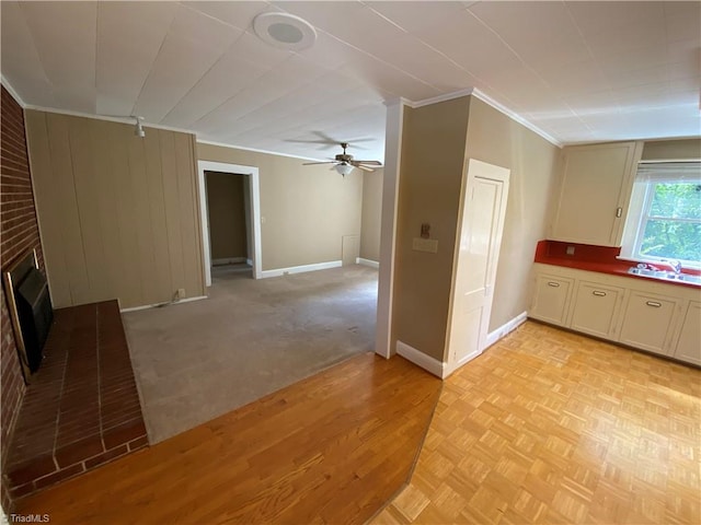 unfurnished living room featuring a brick fireplace, ceiling fan, ornamental molding, sink, and light carpet