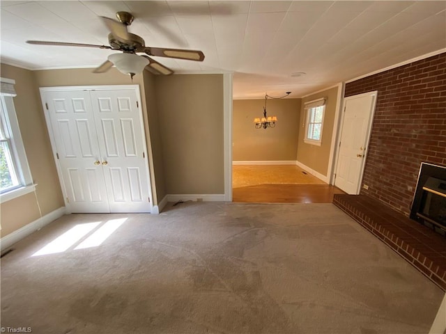 unfurnished living room with ceiling fan with notable chandelier, a wealth of natural light, brick wall, and ornamental molding