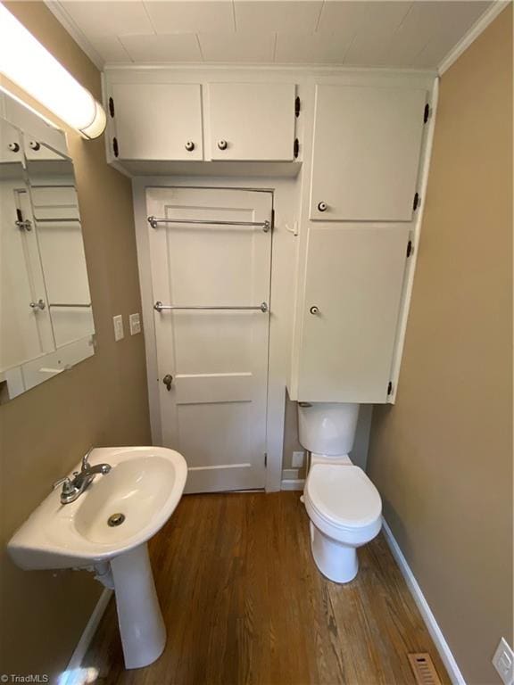 bathroom with wood-type flooring, crown molding, and toilet