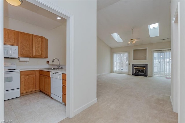 kitchen with light countertops, light carpet, a glass covered fireplace, white appliances, and a sink