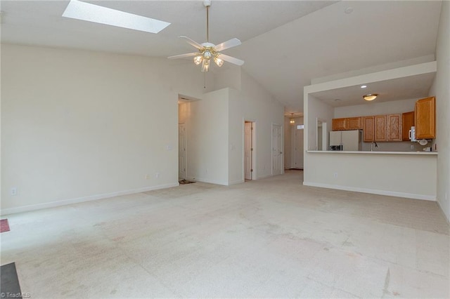 unfurnished living room with baseboards, high vaulted ceiling, a skylight, ceiling fan, and light carpet