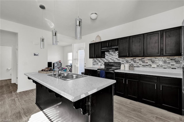 kitchen with sink, black electric range oven, an island with sink, pendant lighting, and light hardwood / wood-style floors