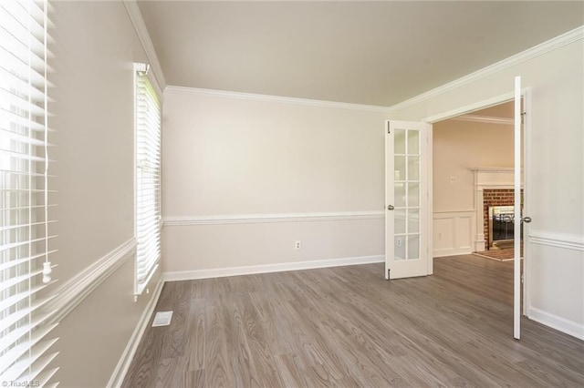 unfurnished room with french doors, ornamental molding, a brick fireplace, and wood finished floors