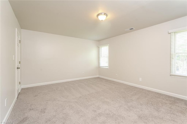 carpeted spare room featuring a healthy amount of sunlight, baseboards, and visible vents
