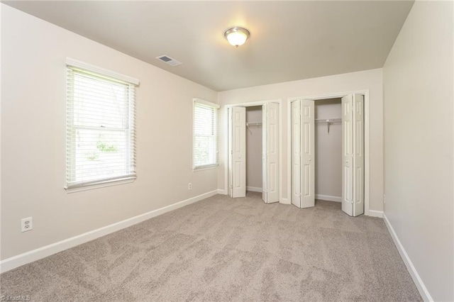 unfurnished bedroom with visible vents, multiple closets, light colored carpet, and baseboards