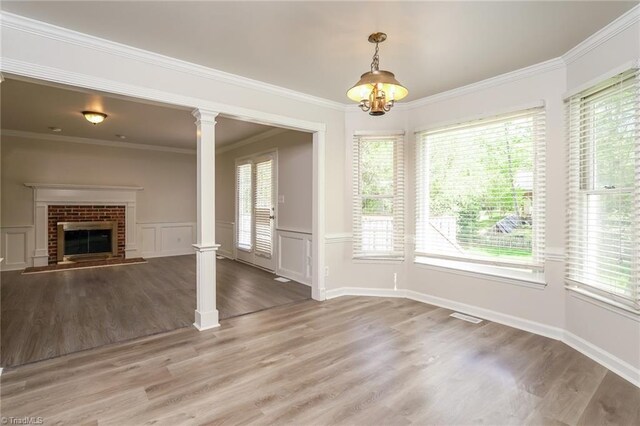 unfurnished living room featuring light wood-style flooring, a healthy amount of sunlight, decorative columns, and a wainscoted wall