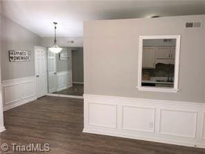 unfurnished room featuring dark wood-style floors, a wainscoted wall, and a decorative wall