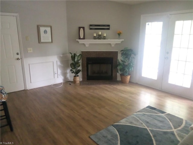 living area with french doors, a fireplace with flush hearth, wainscoting, and wood finished floors