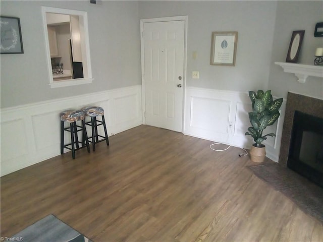 living room featuring wainscoting, wood finished floors, a fireplace with flush hearth, and a decorative wall