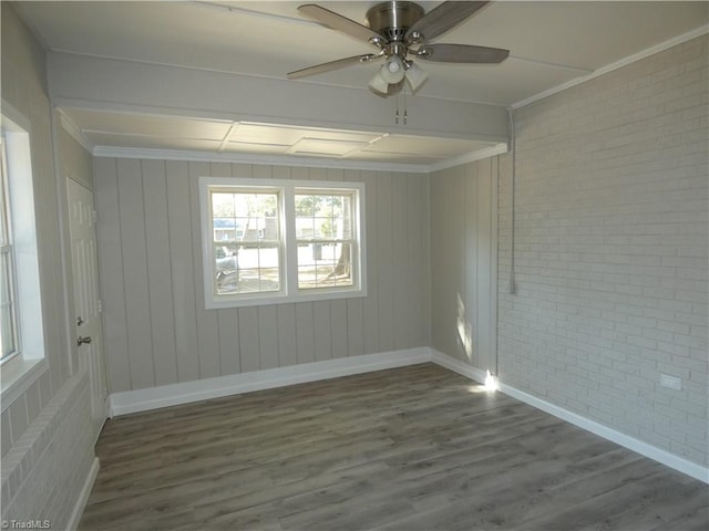 unfurnished room with hardwood / wood-style floors, ceiling fan, ornamental molding, and brick wall