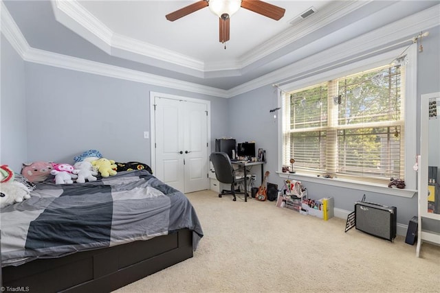 carpeted bedroom with ceiling fan, a raised ceiling, visible vents, ornamental molding, and a closet