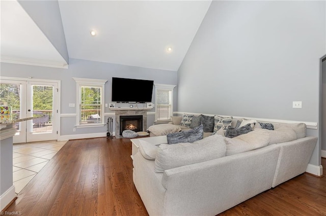 living area featuring wood finished floors, baseboards, high vaulted ceiling, french doors, and a fireplace with flush hearth