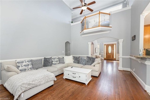 living room featuring a ceiling fan, a towering ceiling, ornate columns, arched walkways, and dark wood finished floors