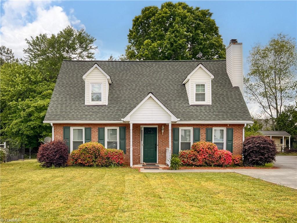 cape cod-style house featuring brick siding, a chimney, roof with shingles, and a front lawn