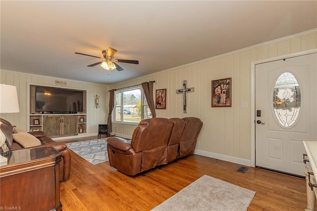 living area with baseboards, ceiling fan, crown molding, and light wood finished floors