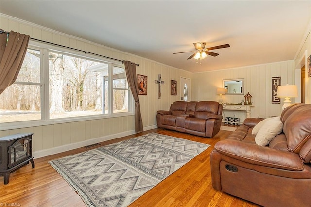 living area featuring visible vents, ornamental molding, a wood stove, and wood finished floors