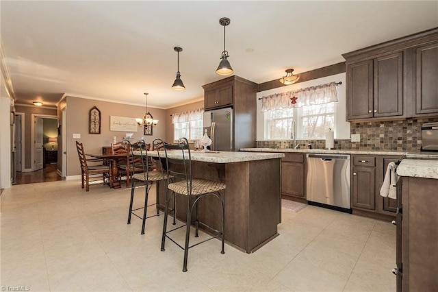 kitchen featuring a breakfast bar, a kitchen island, appliances with stainless steel finishes, decorative backsplash, and light stone countertops