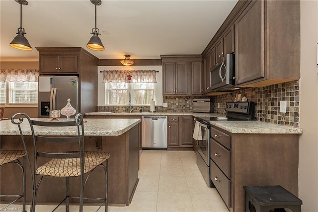 kitchen featuring hanging light fixtures, light countertops, dark brown cabinetry, appliances with stainless steel finishes, and tasteful backsplash