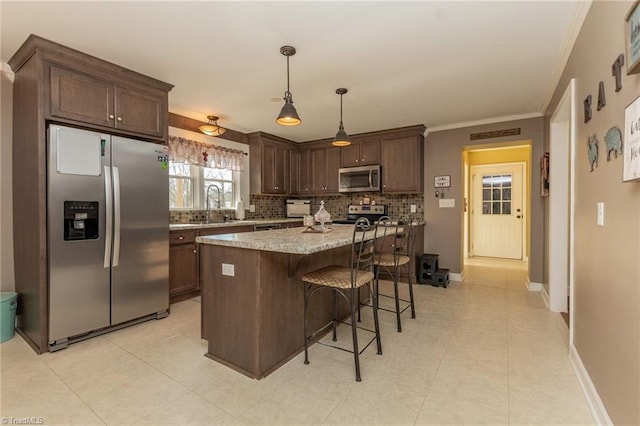 kitchen with a breakfast bar area, ornamental molding, dark brown cabinets, appliances with stainless steel finishes, and backsplash