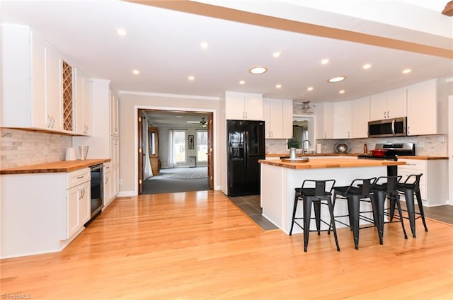 kitchen with stainless steel appliances, wooden counters, white cabinets, and a kitchen bar