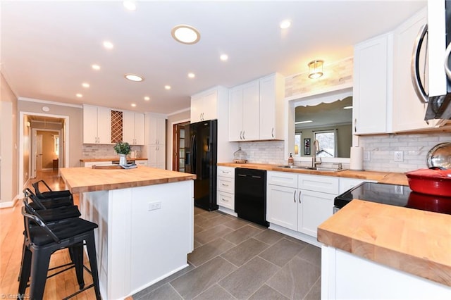 kitchen with butcher block countertops, black appliances, a breakfast bar, and white cabinets