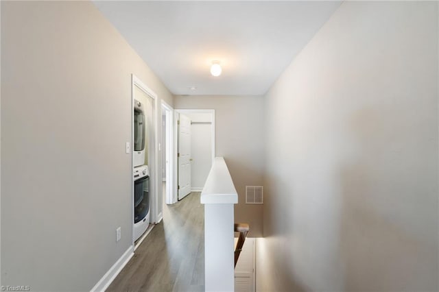 hallway with stacked washer and dryer, baseboards, visible vents, and wood finished floors