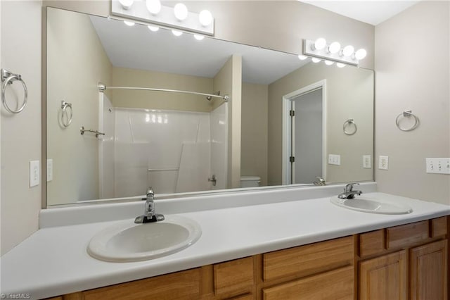 full bathroom with toilet, double vanity, a shower, and a sink