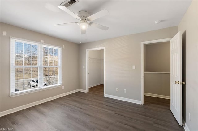 unfurnished bedroom with baseboards, a spacious closet, visible vents, and dark wood-type flooring