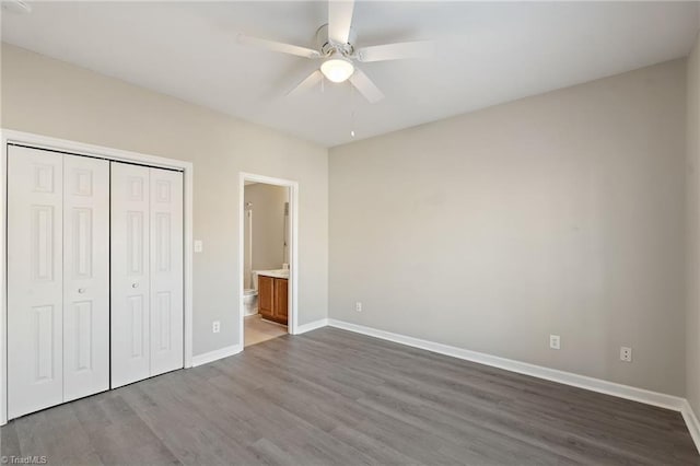 unfurnished bedroom with ceiling fan, connected bathroom, baseboards, a closet, and dark wood-style floors